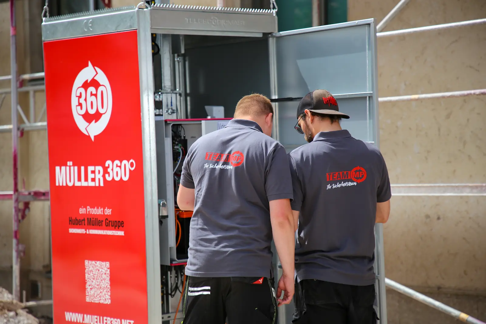 Zwei Techniker der Hubert Müller Gruppe arbeiten an einem geöffneten Müller360-Videoturm auf einer Baustelle.